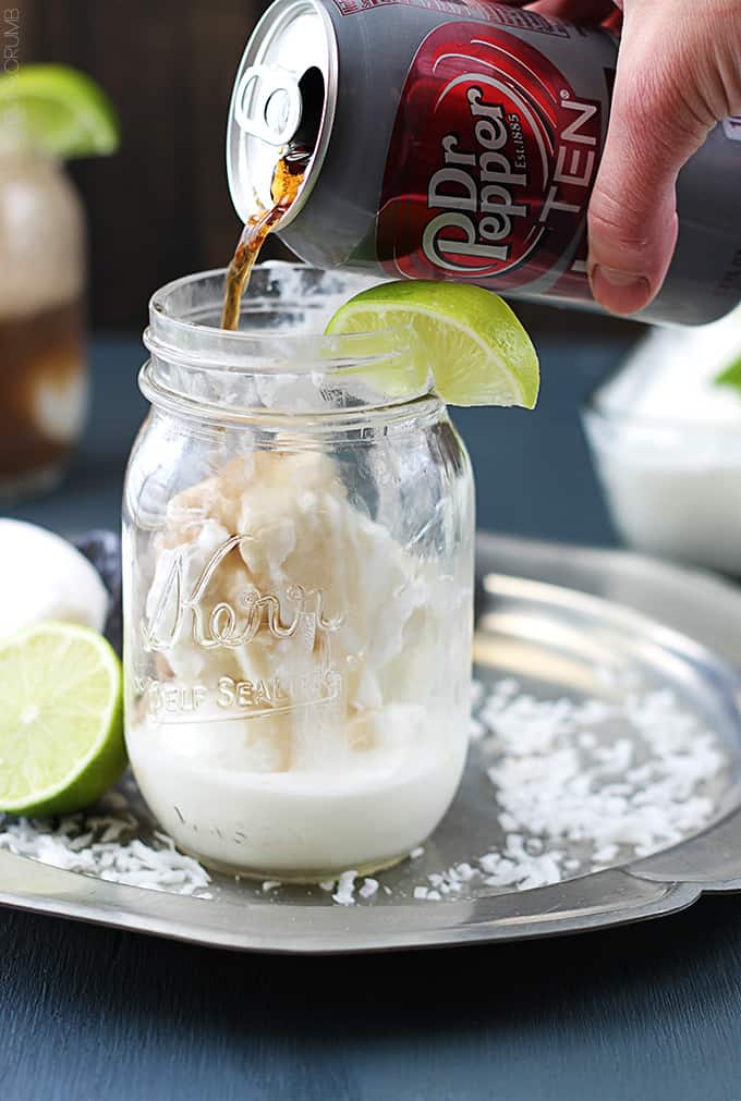 a hand pouring a can of Dr. Pepper into a mason jar with vanilla ice cream in it and a slice of a lime on top.