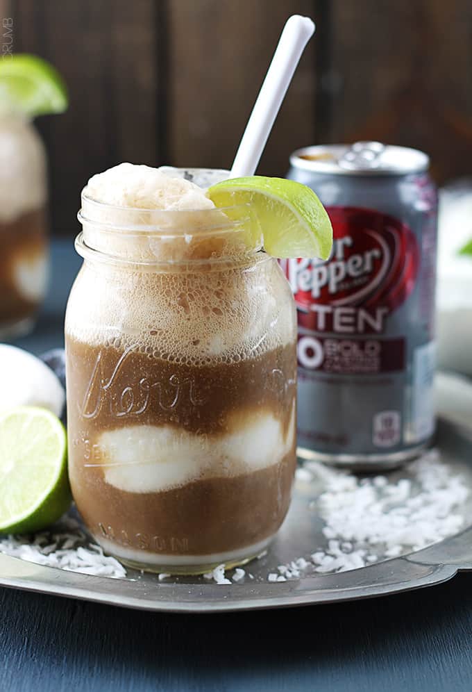 a dirty Dr. Pepper float in a mason jar with a spoon and a slice of a lime on the top with a can of Dr. Pepper in the background.