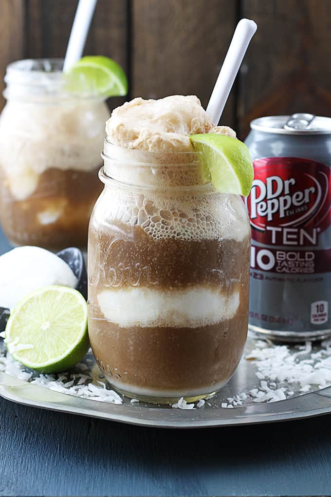 dirty Dr. Pepper floats, a can of Dr Pepper, half of a lime, a scoop of vanilla ice cream on an ice cream scooper, surrounded in coconut shavings on a metal serving tray.