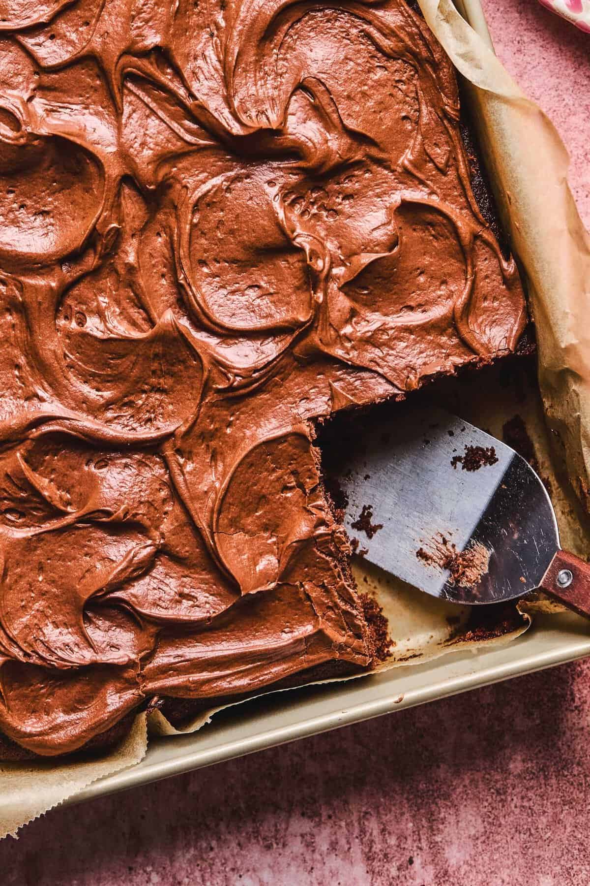 Close up overhead of Dr. Pepper cake in a cake pan with a piece missing.