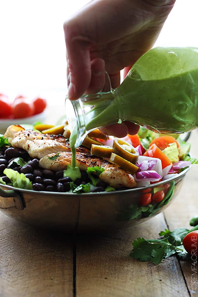 a hand pouring spicy cilantro lime dressing on top of grilled chicken taco salad.