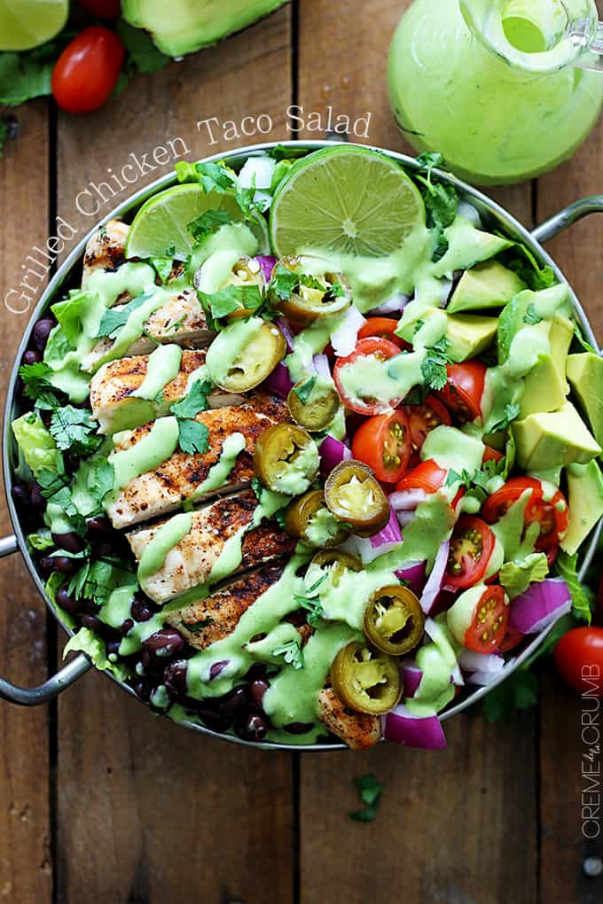 top view of grilled chicken taco salad with spicy cilantro lime dressing in a metal bowl with the title of the recipe written around the bowl on the top left side. 