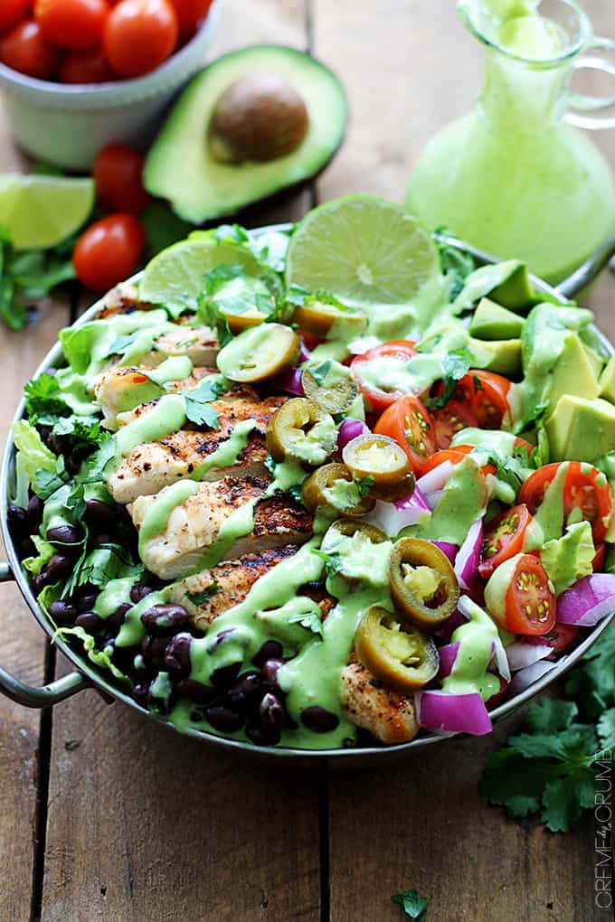 grilled chicken taco salad with spicy cilantro lime dressing in a metal bowl with more toppings in the background.