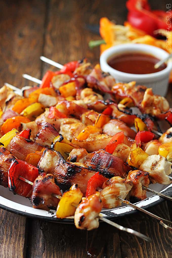 side view of grilled honey bbq bacon chicken kabobs on a plate with bbq sauce in a bowl on the side.