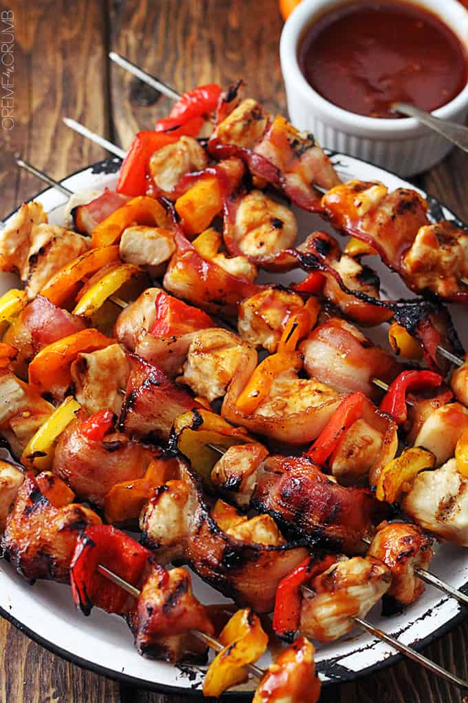 top view of grilled honey bbq bacon chicken kabobs on a plate with bbq sauce in a bowl on the side.