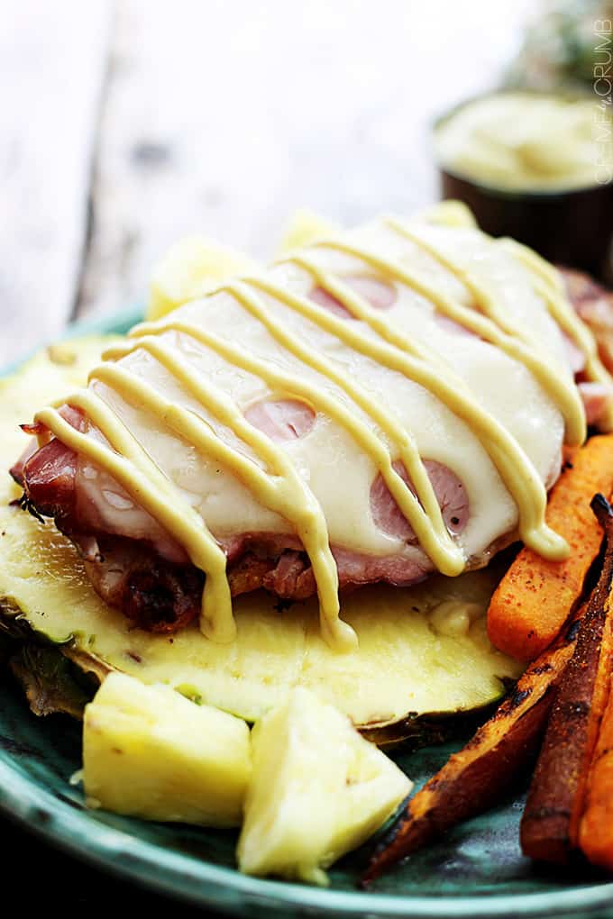 grilled Malibu chicken on half of a pineapple on a plate with chunks of pineapple and sweet potato fries.