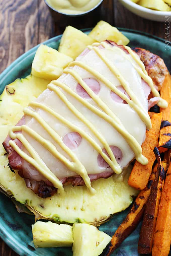 close up top view of grilled Malibu chicken on half of a pineapple on a plate with pineapple chunks and sweet potato fries.