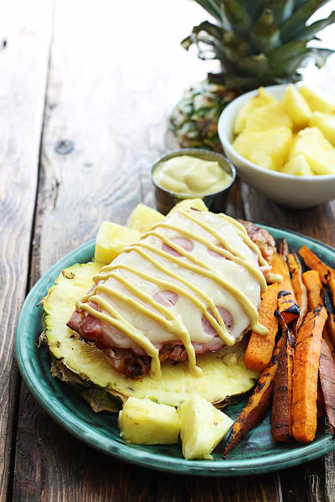 grilled Malibu chicken on half of a pineapple on a plate with pineapple chunks and sweet potato fries.