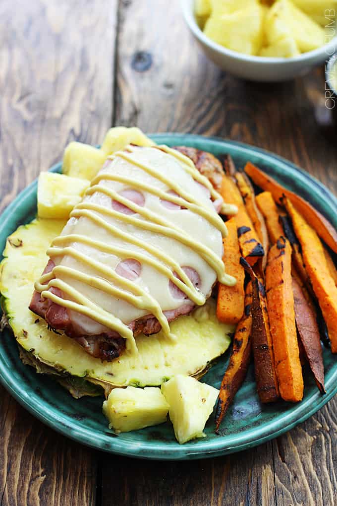 grilled Malibu chicken on half of a pineapple on a plate with pineapple chunks and sweet potato fries.