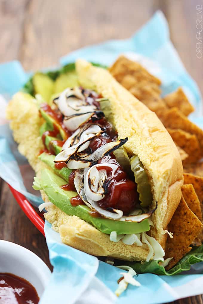 bbq hot dog with avocado & grilled onions with a side of chips on a lunch tray.