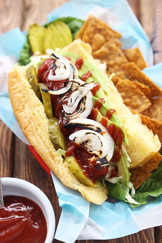 bbq hot dog with avocado & grilled onions with a side of chips on a lunch tray.