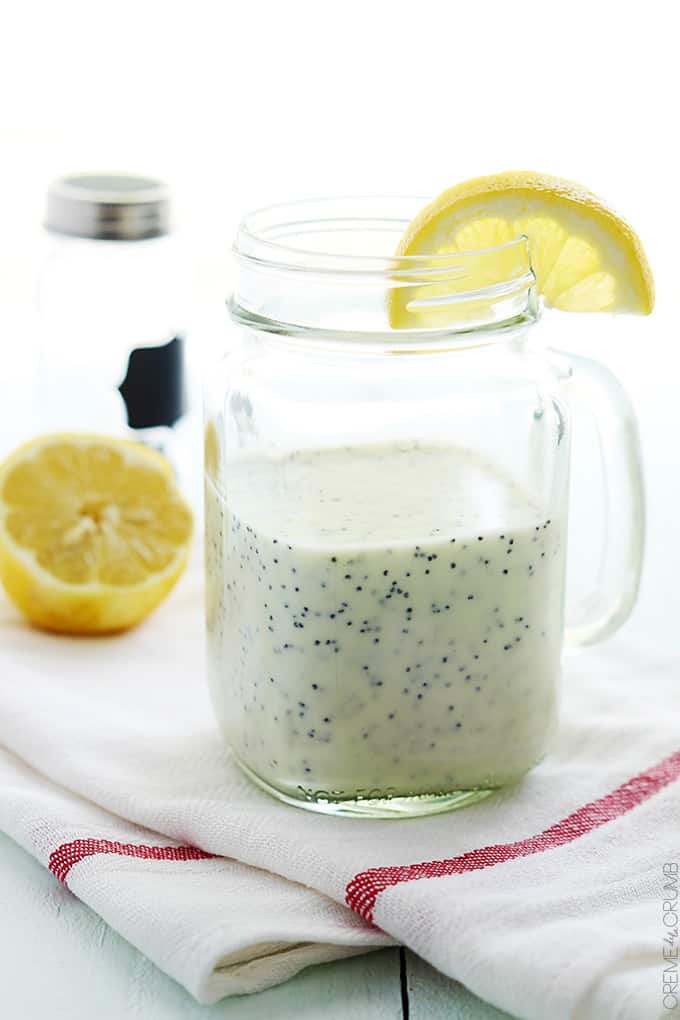 lemon poppyseed dressing in a mason jar with a handle and a slice of lemon on the top on a cloth napkin.