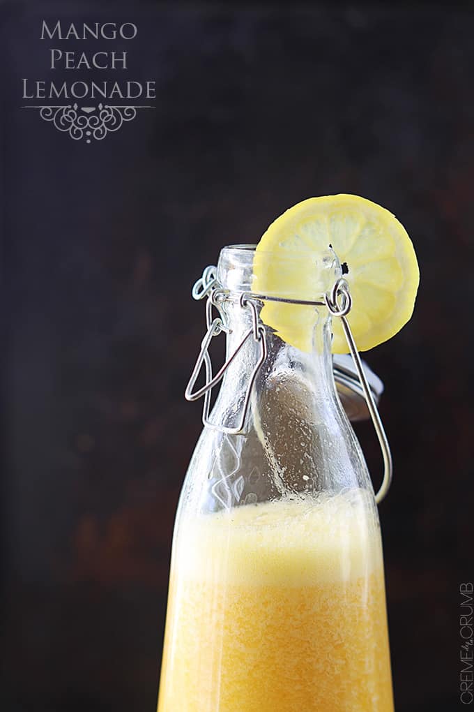 an old fashion milk bottle full of mango peach lemonade with a slice of lemon on the top with the title of the recipe written on the top left corner of the image.