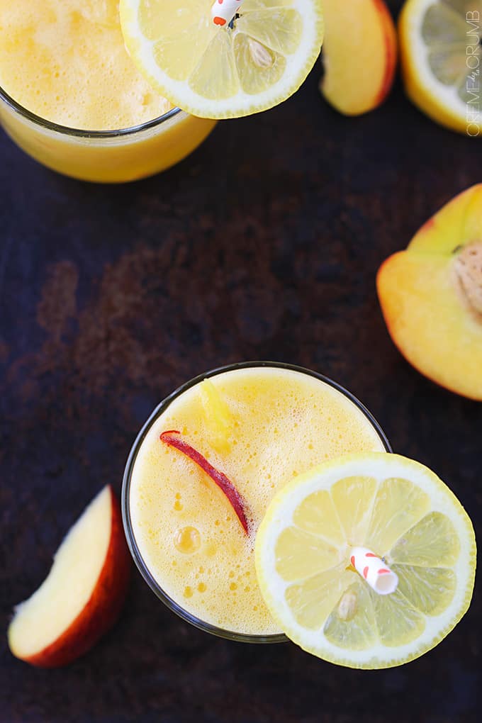 top view of a couple glasses of mango peach lemonade with slices of lemon on the straws with slices of mango and lemon on the side.