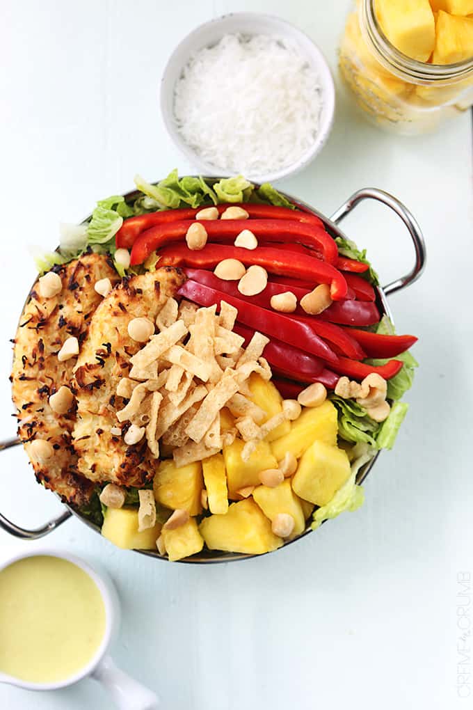 top view of Pina Colada chicken salad in a metal bowl with Pina Colada vinaigrette, coconut shavings, and pineapple chunks on the side.