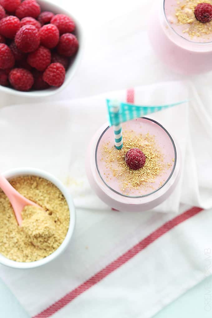 top view of a raspberry cheesecake smoothie in a glass with raspberries and crushed graham cracker in bowls on the side.