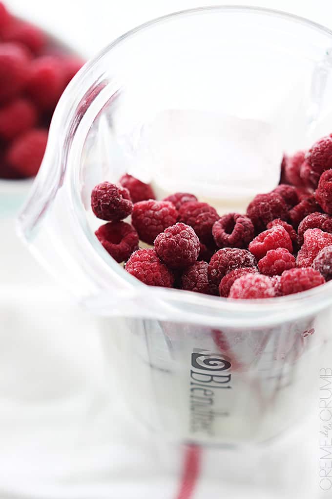 raspberries in a blender with more raspberries in a bowl faded in the background.