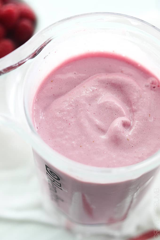 raspberry cheesecake smoothie in a blender with raspberries in a bowl faded in the background.