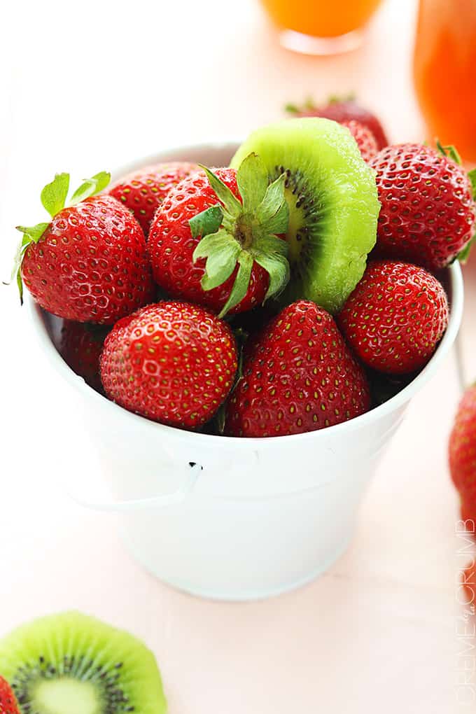 a white metal tin full of strawberries with a slice of a kiwi on top.