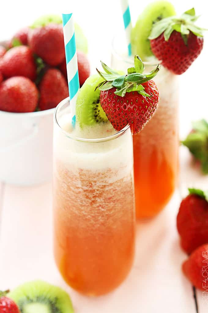 two glasses of strawberry kiwi lemonade with a slice of kiwi and a whole strawberry on the top of the glass with a straw and a bowl of strawberries in a bowl on the side.