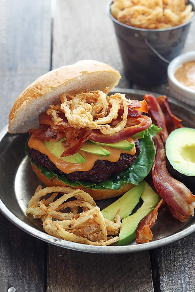 a western bacon burger with bbq mayo and crispy onion strings on a metal plate with more burger toppings on the side.