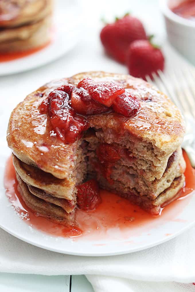 close up of a stack of whole wheat strawberry pancakes on a plate with some of the pancakes missing.