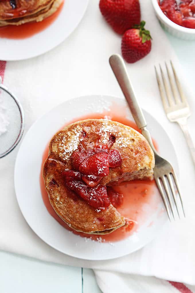 top view of a stack of whole wheat strawberry pancakes on a plate with some of the pancakes missing and a fork on the side.