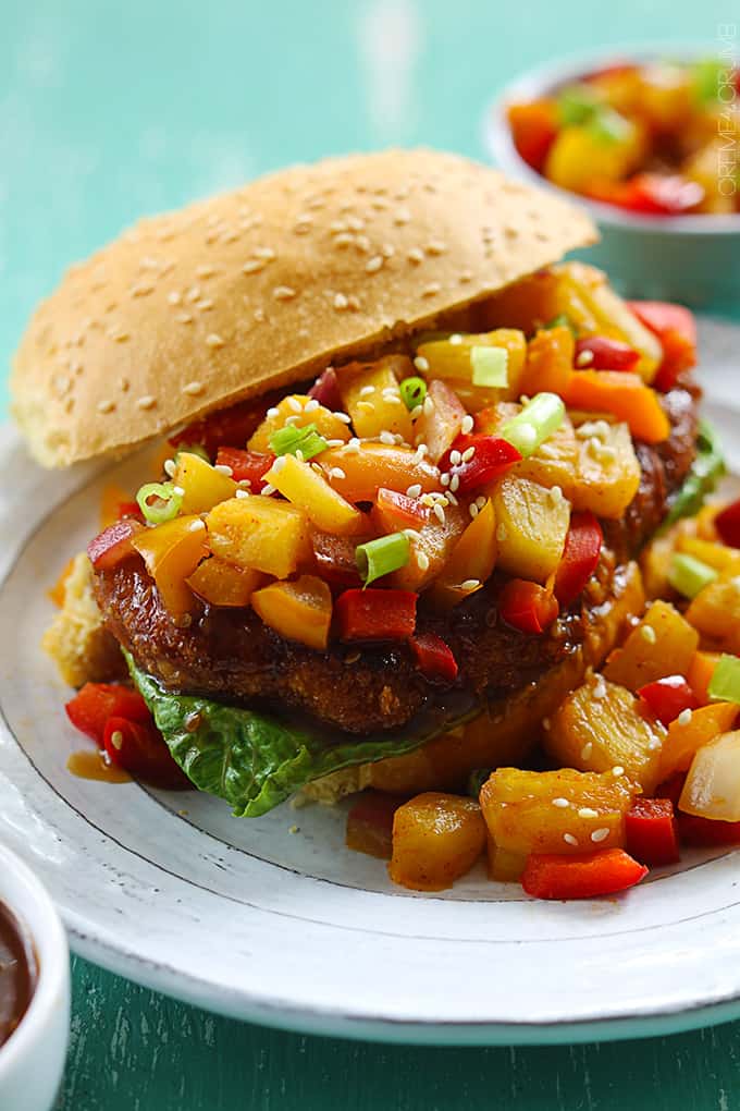 an an aloha chicken sandwich on a plate with pineapple salsa in a small bowl faded in the background.