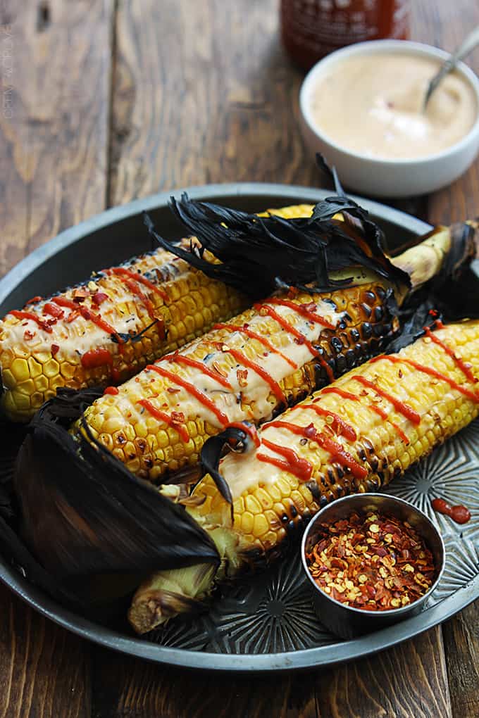Asian grilled corn on a serving tray with seasoning and sauce in bowls on the side.