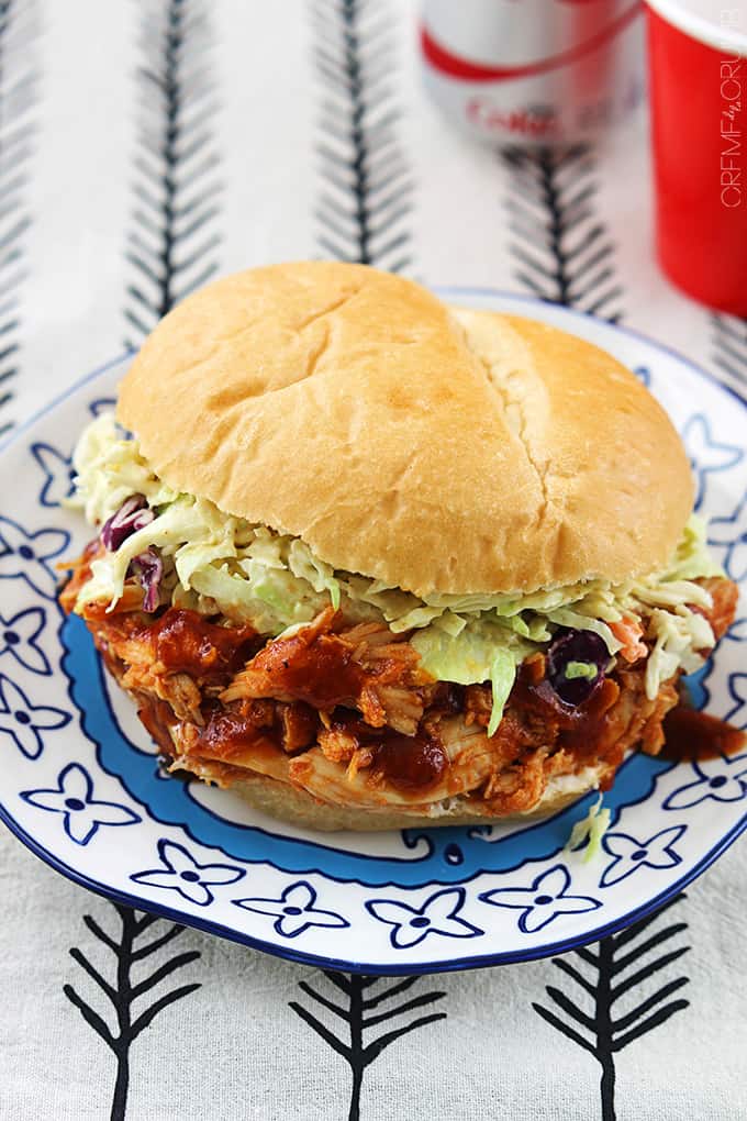 top view of a slow cooker bbq pulled chicken sandwich  on a plate with soda faded in the background.