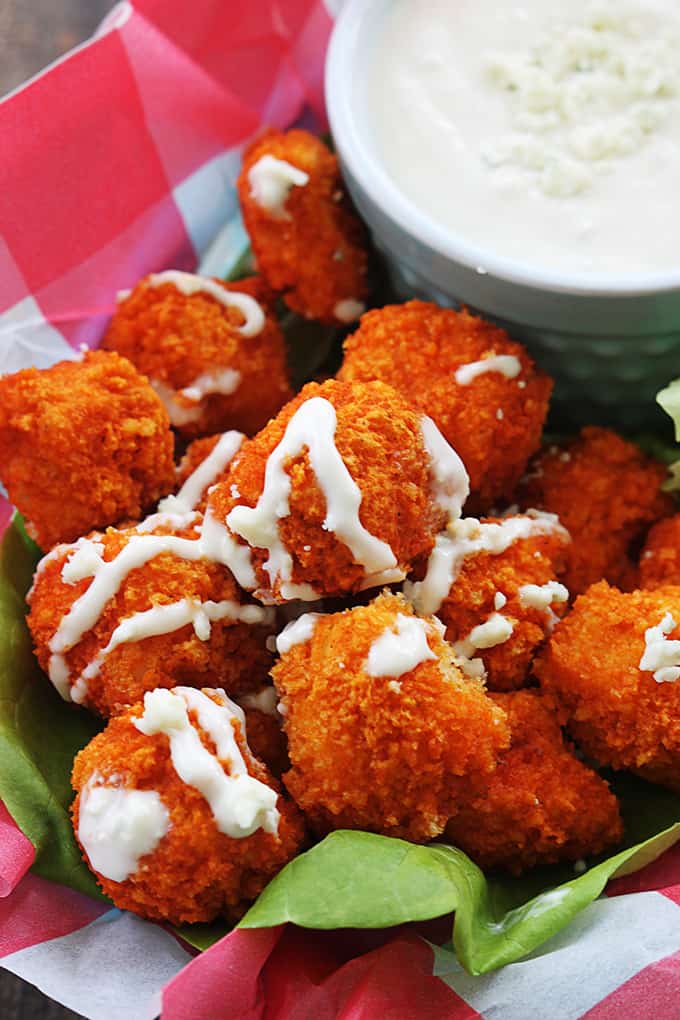 close up of buffalo popcorn chicken in a basket with sauce on top and in a bowl on the side.