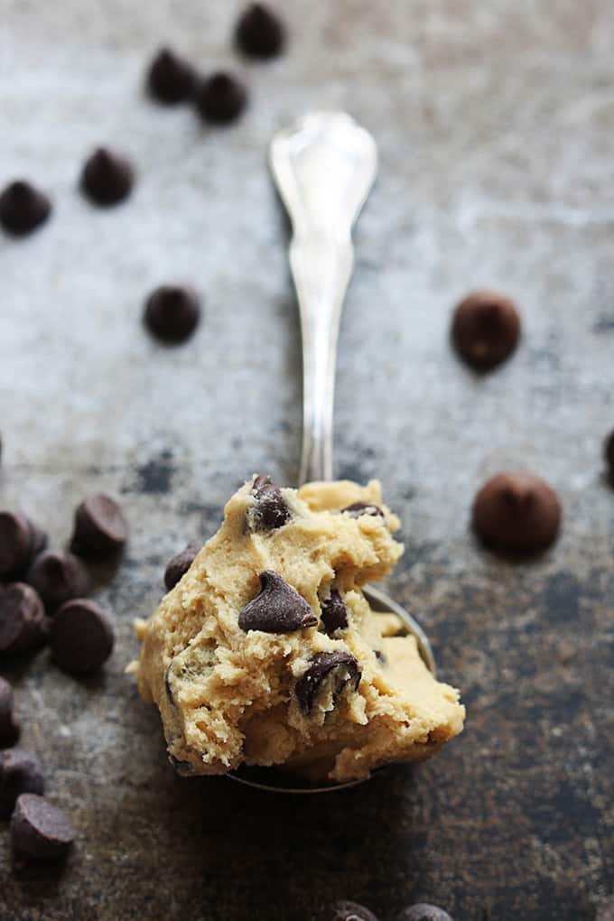 a spoon with a scoop of chocolate chip cookie dough on it with more chocolate chips surrounding it.