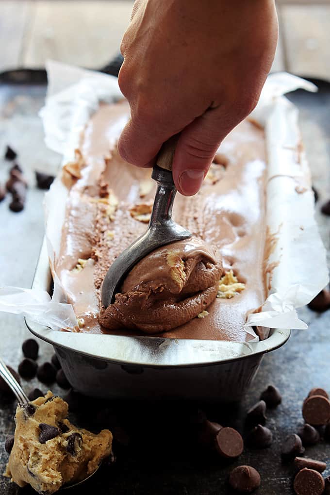 chocolate cookie dough ice cream in a tray with a hand scooping some out with an ice cream scooper.