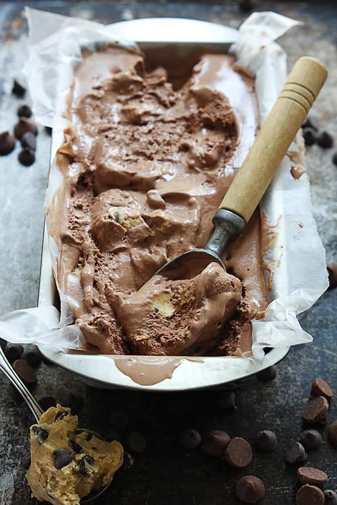 chocolate cookie dough ice cream with an ice cream scooper in a tray with a spoon of cookie dough and chocolate chips on the side.