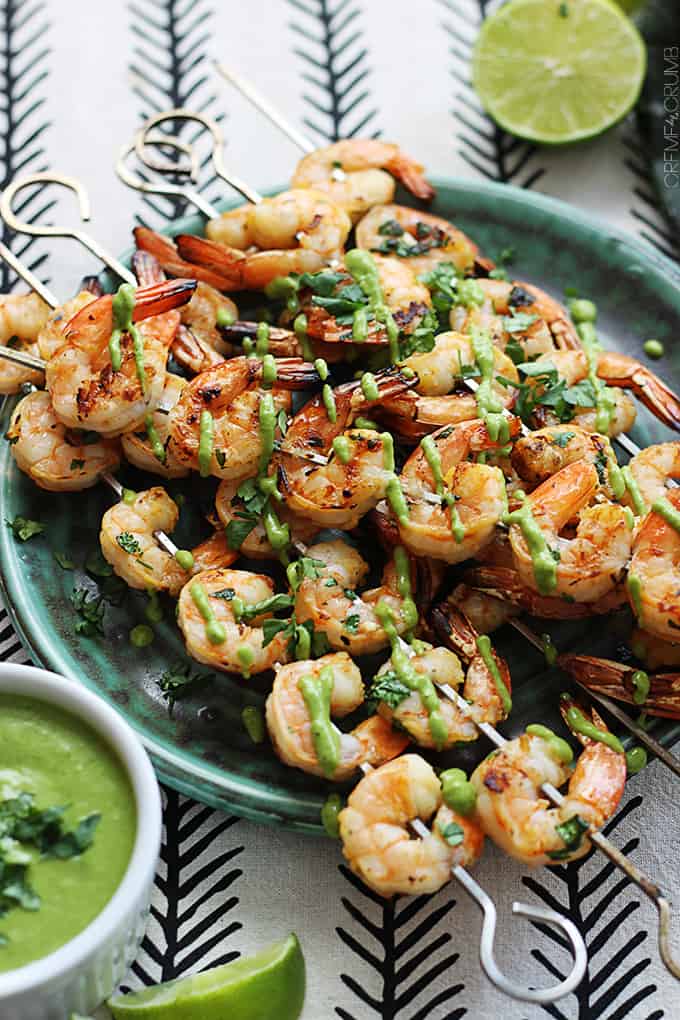 cilantro lime grilled shrimp + roasted poblano sauce skewers on a plate with more sauce and half of a lime on the side.
