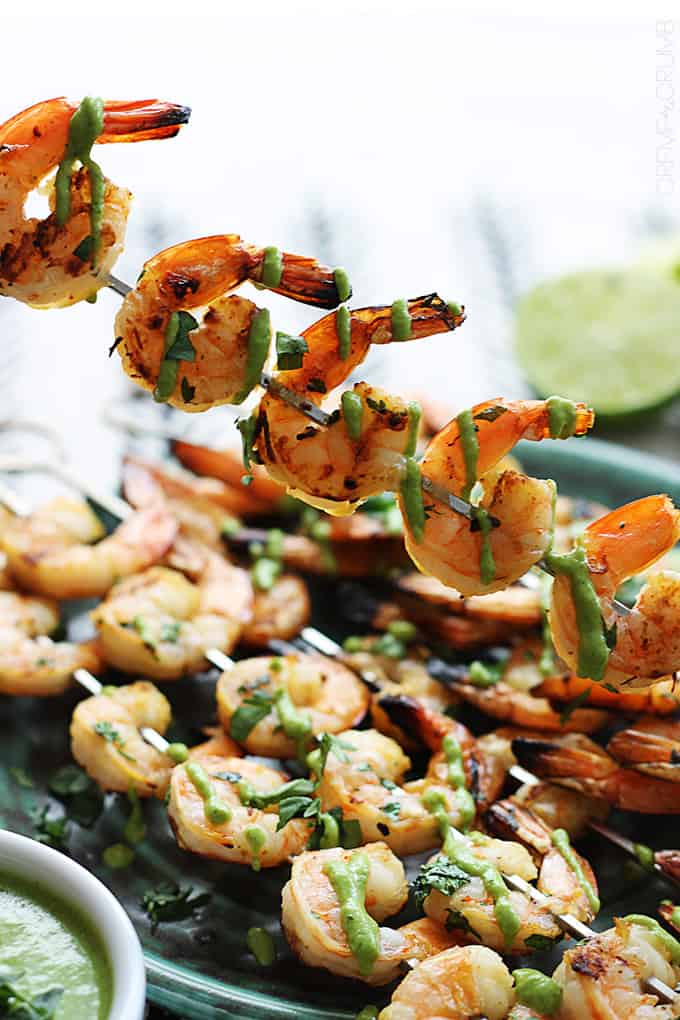 a cilantro lime grilled shrimp skewer with roasted poblano sauce being held above more shrimp skewers on a plate.