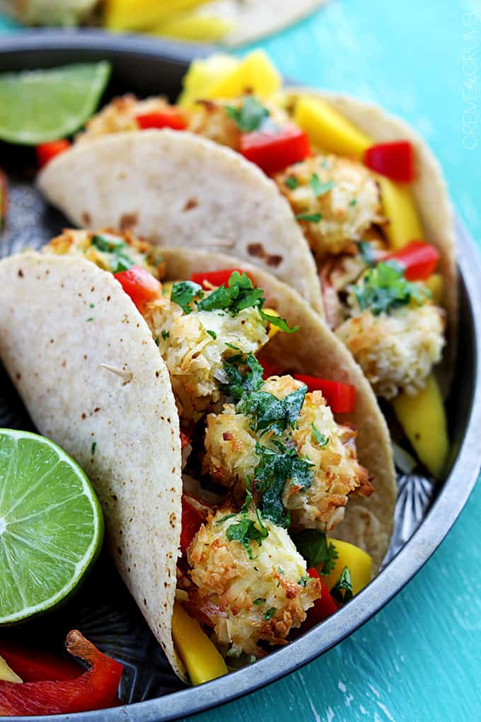 coconut shrimp tacos on a metal tray with limes on the side.