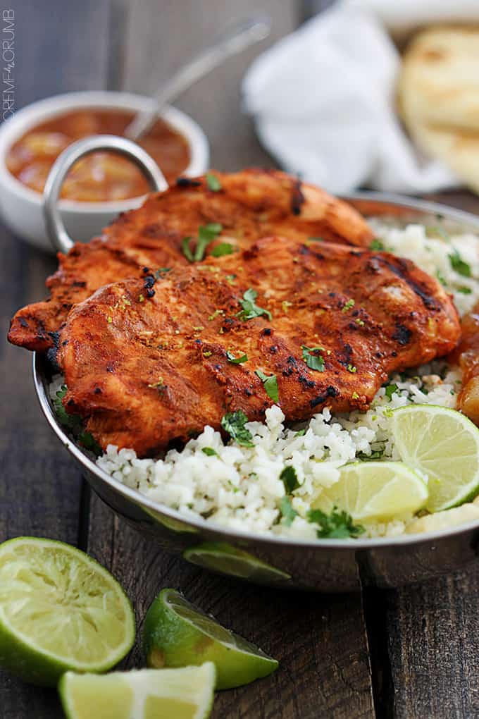 grilled tandoori chicken with rice and slices of lime on a metal tray with more limes and sauce on the side.