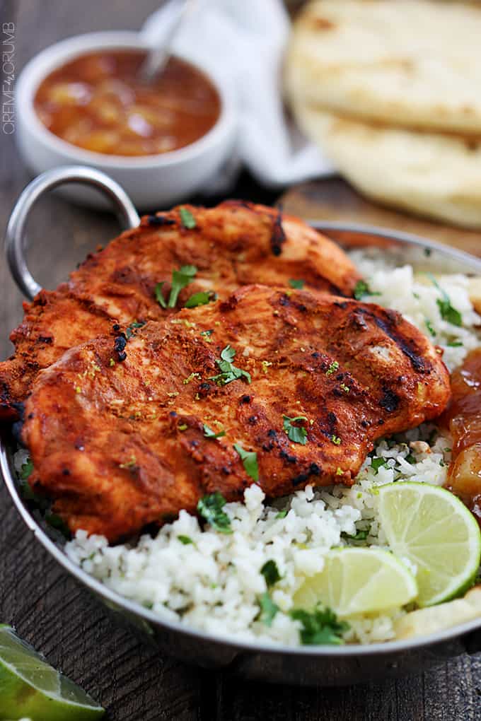 grilled tandoori chicken with rice and slices of limes in a metal tray.