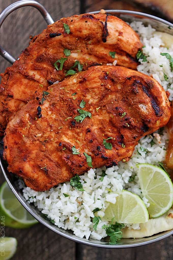 top close up view of grilled tandoori chicken with rice and limes in a metal tray.