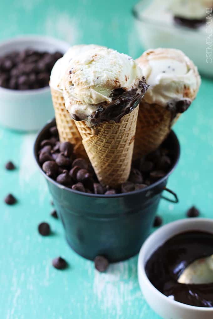 hot fudge ripple mint chocolate chip ice cream cones in a metal tin full of chocolate chips with more chocolate chips and chocolate sauce on the side.