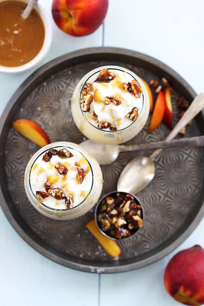 top view fo two peaches n' cream caramel pecan milkshakes on a serving tray surrounded with spoons and toppings.