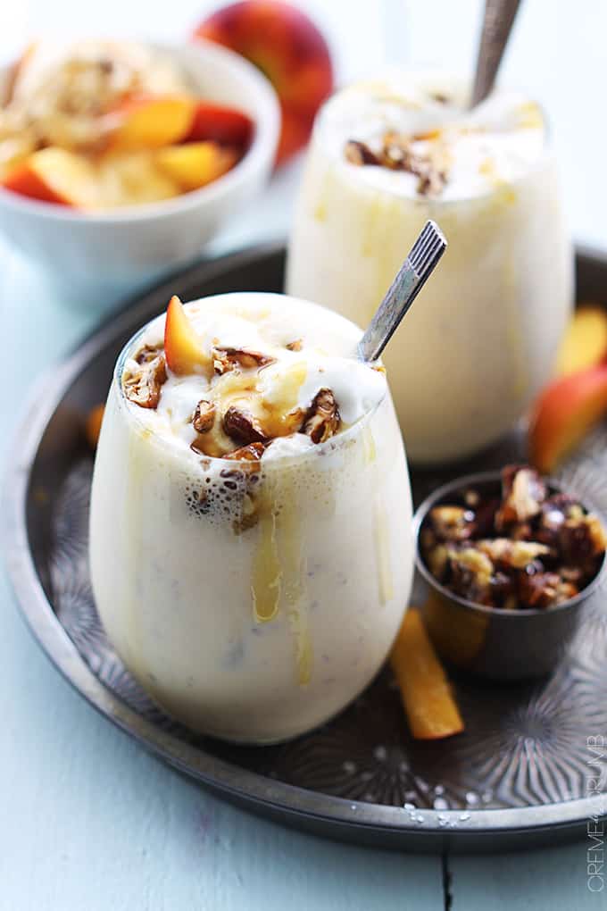 a peaches n' cream caramel pecan milkshake in a glass on a serving tray with another milkshake and toppings faded in the background.