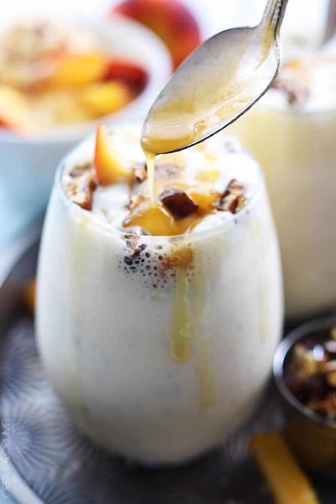 a peaches n' cream caramel pecan milkshake in a glass with a spoon pouring caramel on top.