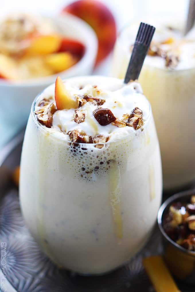 a peaches n' cream caramel pecan milkshake in a glass with another milkshake and toppings faded in the background.