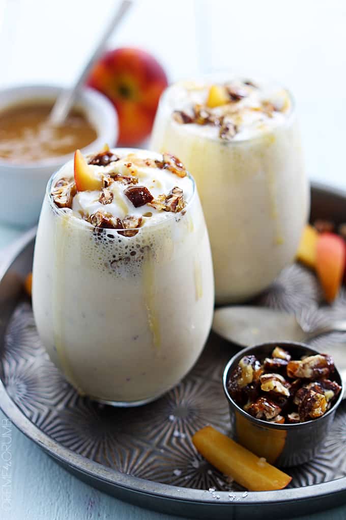 two peaches n' cream caramel pecan milkshakes in glasses on a serving tray with toppings on the side and faded in the background.