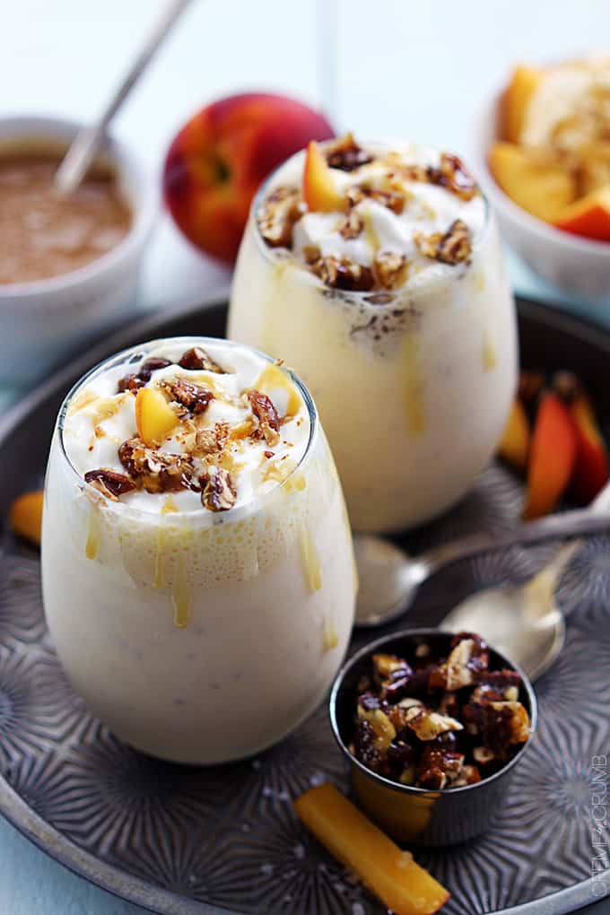 peaches n' cream caramel pecan milkshakes on a serving tray surrounded with spoons and toppings.