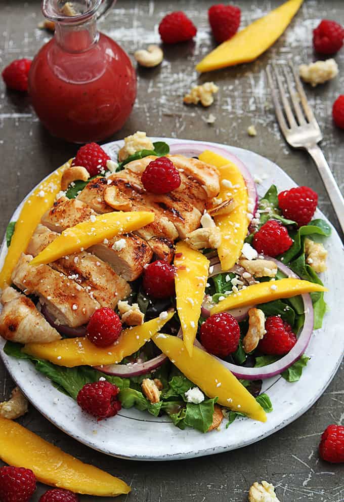 top view of raspberry mango chicken cashew salad on a plate with a fork, raspberry vinaigrette and fruit on the side.