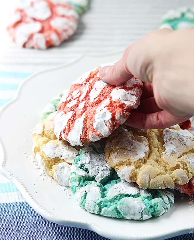 a hand taking a red white + blue crinkle cookie from a plate of cookies with more cookies faded in the background.