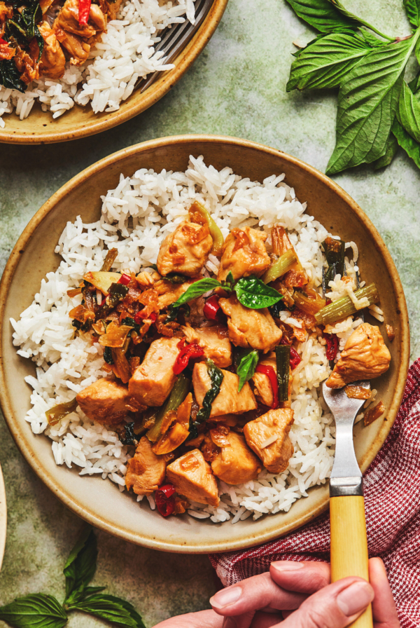 overhead view of one whole and one partial bowl of stir fry chicken with basil over rice.